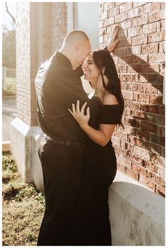 a man and woman standing next to each other near a brick wall with their arms around each other