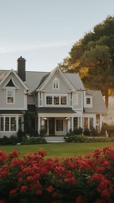 a large white house with red flowers in the front yard