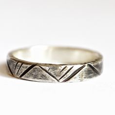 a silver ring with an arrow design on the front and side, sitting on a white surface