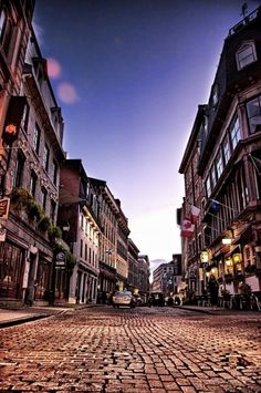 an empty cobblestone street in the middle of town at dusk with buildings lining both sides