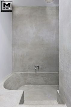 a white bathroom with a tub and shower head in it's corner, surrounded by concrete walls