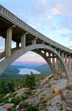 a wooden bridge spanning over a mountain with a lake in the background