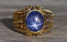 The Lilburn Men's Signed 18K Yellow Gold Cocktail Ring set with Star Sapphire. Crafted in 18 karat yellow gold, this vintage men's ring centers on a bezel set blue star sapphire. Original engraving and scroll work is present throughout this ring. The ring is signed by the maker who is likely Carter and Gough. The ring is currently a finger size 7.75 and is able to be resized for an additional charge. Each piece has been hand selected and meticulously identified and graded by a Graduate Gemologis Blue Star Sapphire Rings For Men, Vintage Gold Sapphire Ring With Bezel Setting, Vintage Gold Sapphire Ring With Polished Finish, Celestial Yellow Gold Signet Ring For Formal Occasions, Diamond Star Necklace, Yellow Gold Cocktail Ring, Southwest Usa, Star Sapphire Ring, Blue Star Sapphire