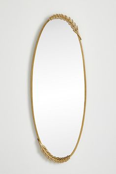 an oval mirror hanging on the wall with gold trimmings and leaves around it