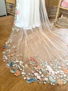 a wedding veil with flowers on it sitting on a wooden floor next to a chair