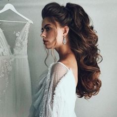 a woman standing in front of a wedding dress with her hair pulled back into a pony tail