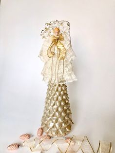 a gold and white christmas tree made out of shells with a doll in the top