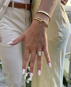 a woman with white nails and a ring on her finger next to a man in beige pants