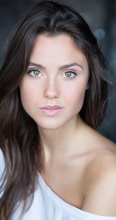 a woman with long brown hair and green eyes is posing for a studio photo wearing a white shirt