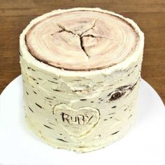 a white plate topped with a cake covered in frosting next to a tree trunk