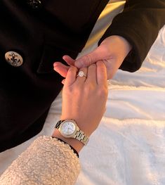 a person holding the hand of another person with a watch on their wrist and wearing a black jacket