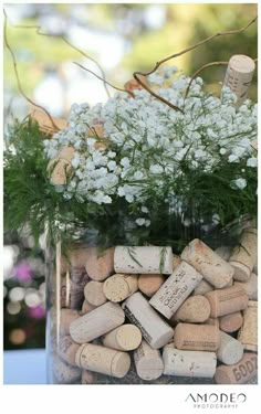 a vase filled with lots of wine corks next to white flowers and greenery