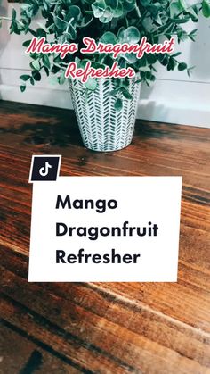 a plant sitting on top of a wooden table next to a sign that says mango dragonfruit refresher