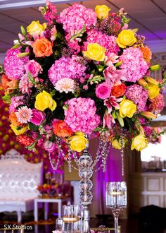 a tall vase filled with lots of colorful flowers on top of a table next to candles