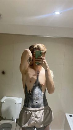 a man taking a selfie in front of a bathroom mirror with tattoos on his body