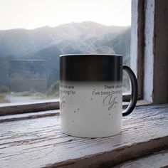 a black and white coffee mug sitting on top of a wooden table next to a window