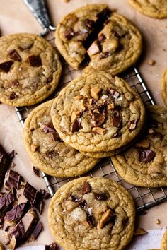 chocolate chip cookies cooling on a wire rack with chopped nuts and other toppings next to them