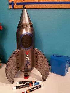 a toy rocket ship sitting on top of a table next to crayons and markers