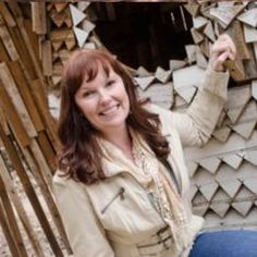 a woman standing in front of a wooden structure holding her hand up to the side