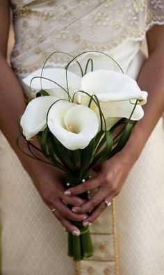 a woman holding a bouquet of white flowers in her hands and wearing a wedding dress