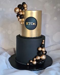 a black and gold wedding cake with pearls on the top is adorned with a ktc logo