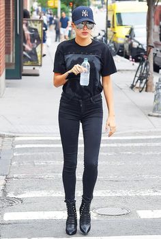 a woman walking across a cross walk holding a water bottle and cell phone in her hand