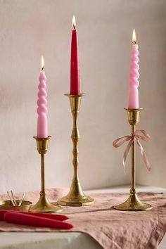 three candles are sitting on a table next to a red pen and pink napkins