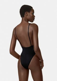 a woman in a black swimsuit with her back turned to the camera, looking down