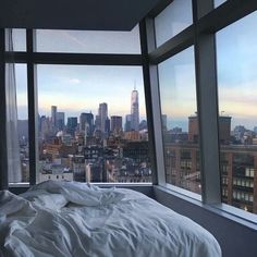 an unmade bed in front of large windows overlooking the cityscape and skyscrapers