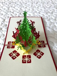 a card with a christmas tree on it and presents under the tree is cut out from paper