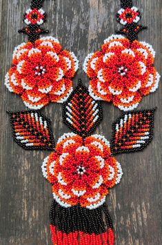 an orange and black beaded necklace with flowers on it, sitting on a wooden surface