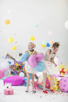 two young women standing next to each other in front of balloons and confetti