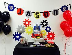 a birthday party with balloons, cake and decorations on a table in front of a white wall