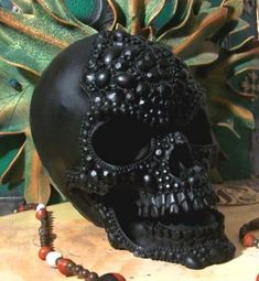 a black skull is sitting on a table next to some beads and a beaded necklace