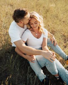 a man and woman sitting on the ground hugging each other in an open grassy field