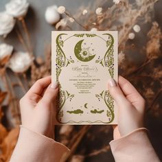 a person holding up a wedding card with the moon and stars on it in front of some dried flowers