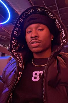 a young man wearing a hoodie standing in front of a neon sign