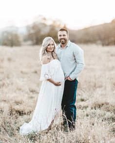 a pregnant couple standing in the middle of a field