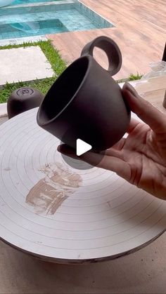 a person is holding a coffee cup over a table with a pool in the background