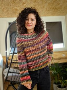 a woman standing in front of a bed wearing a multicolored knitted sweater