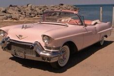 an old pink convertible car parked on the beach