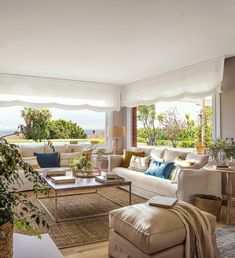 a living room filled with lots of furniture next to a large open window overlooking the ocean