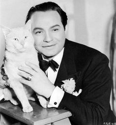 a man in a tuxedo holding a cat on top of a wooden table