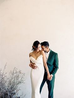 a man and woman standing next to each other in front of a white wall holding hands