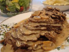 a plate topped with meat and gravy next to a bowl full of salad