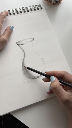 a woman is drawing a vase with pencils on a piece of paper next to a cup