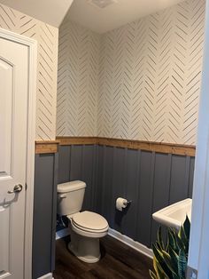 a white toilet sitting inside of a bathroom next to a wooden floor and wallpaper