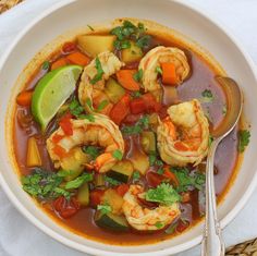 mexican shrimp soup in a white bowl with a spoon on the side and green background