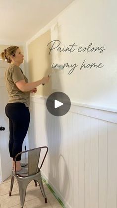 a woman is painting the wall in her house with white paint and she is standing on a chair