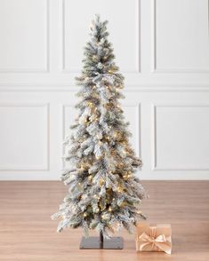 a small white christmas tree with lights on it and a present in the foreground